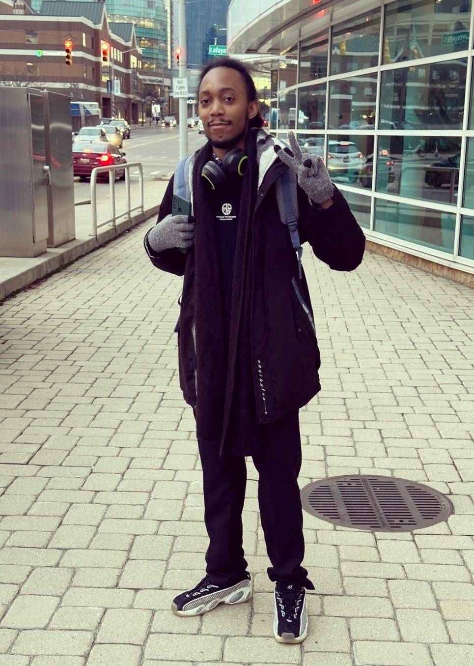 Geofrey standing in front of a downtown building, giving a peace sign with his hand